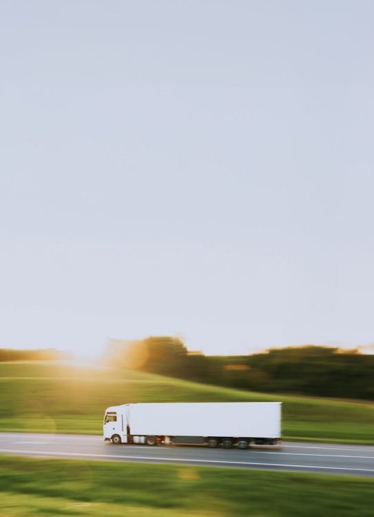 photo by artem balashevsky White cargo truck speeding through Vitebsk countryside at sunrise, symbolizing transportation and logistics.